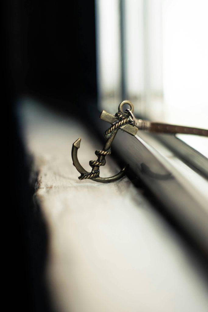 Soft focus of metal stylish charm in anchor shape with leather strap placed on grunge windowsill