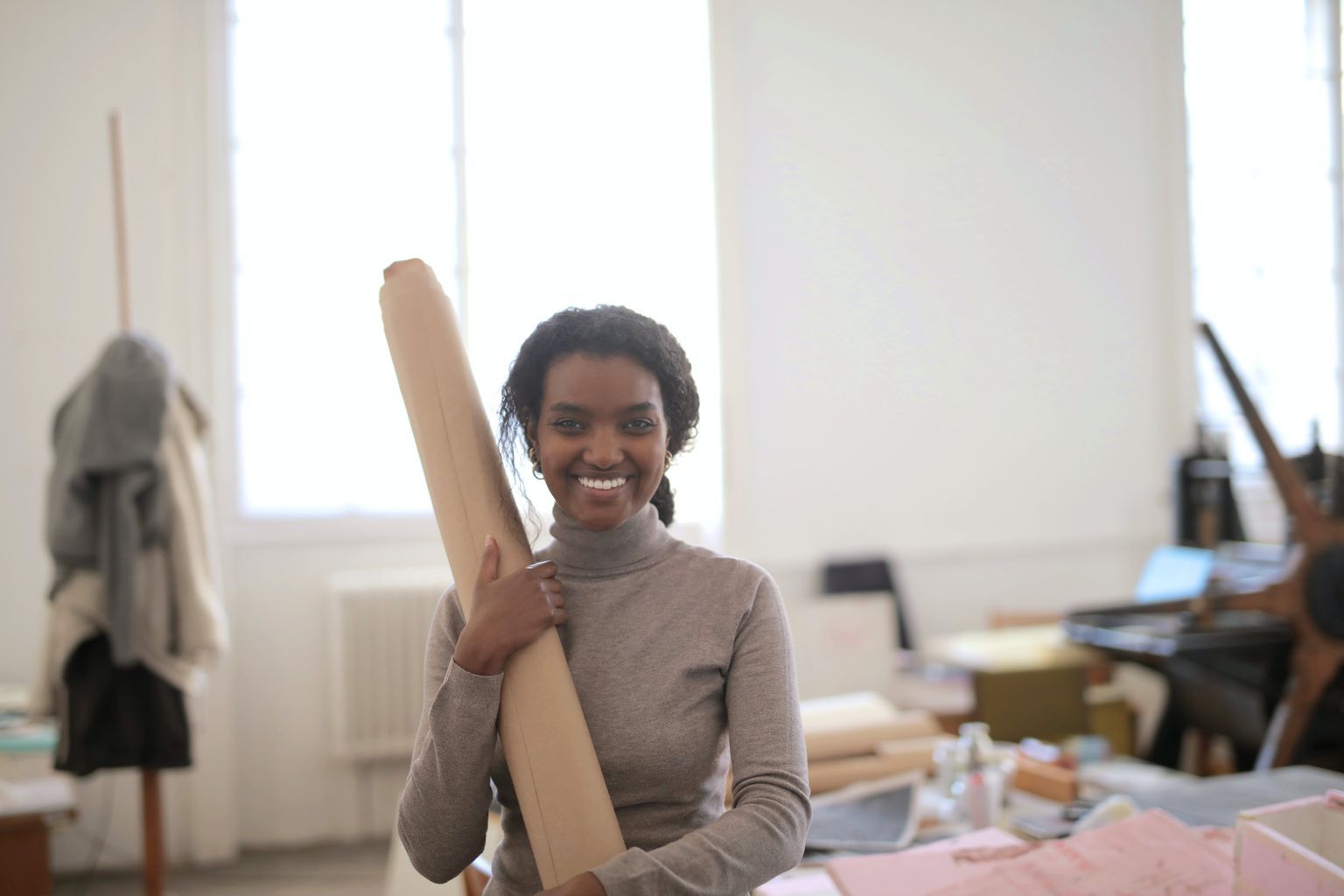 Cheerful young ethnic female worker wearing casual clothes standing with paper roll while working in modern spacious workshop