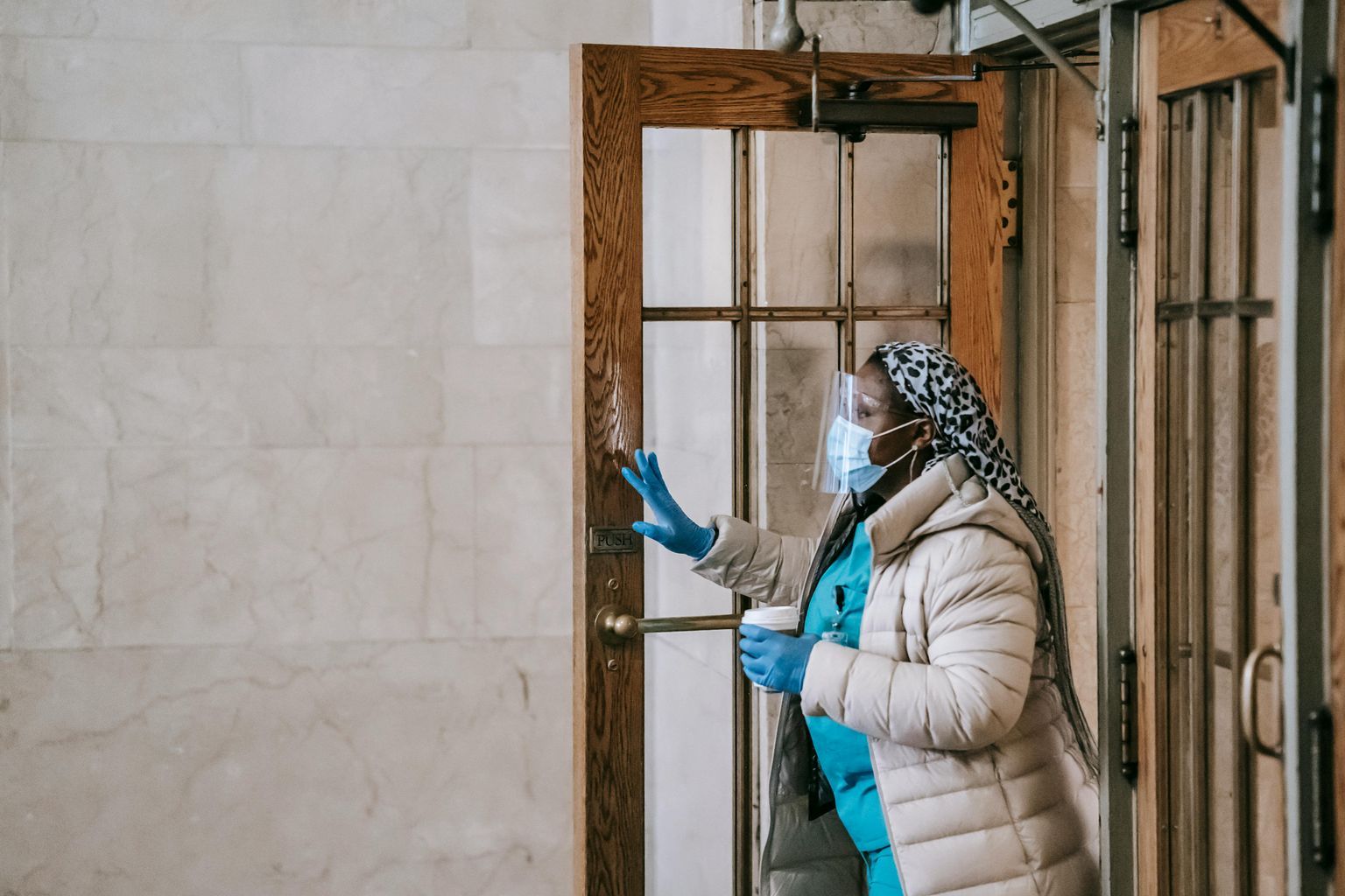 Black nurse in respirator and gloves leaving modern building