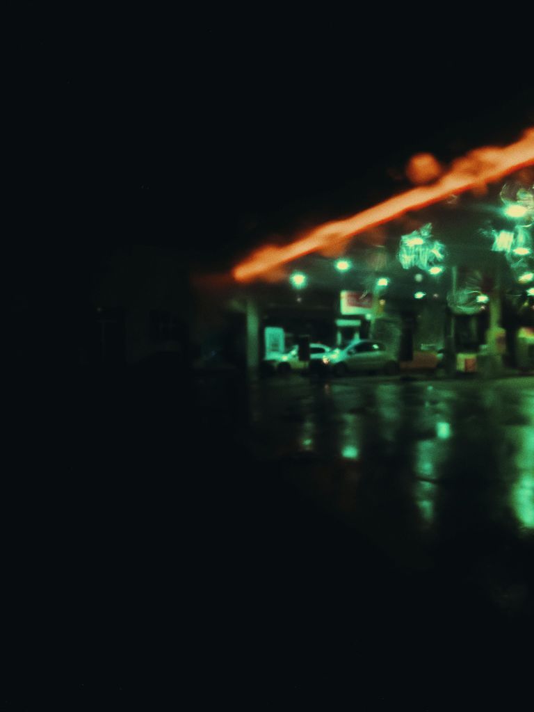 Defocused cars on gas station with neon illumination at night in rainy weather