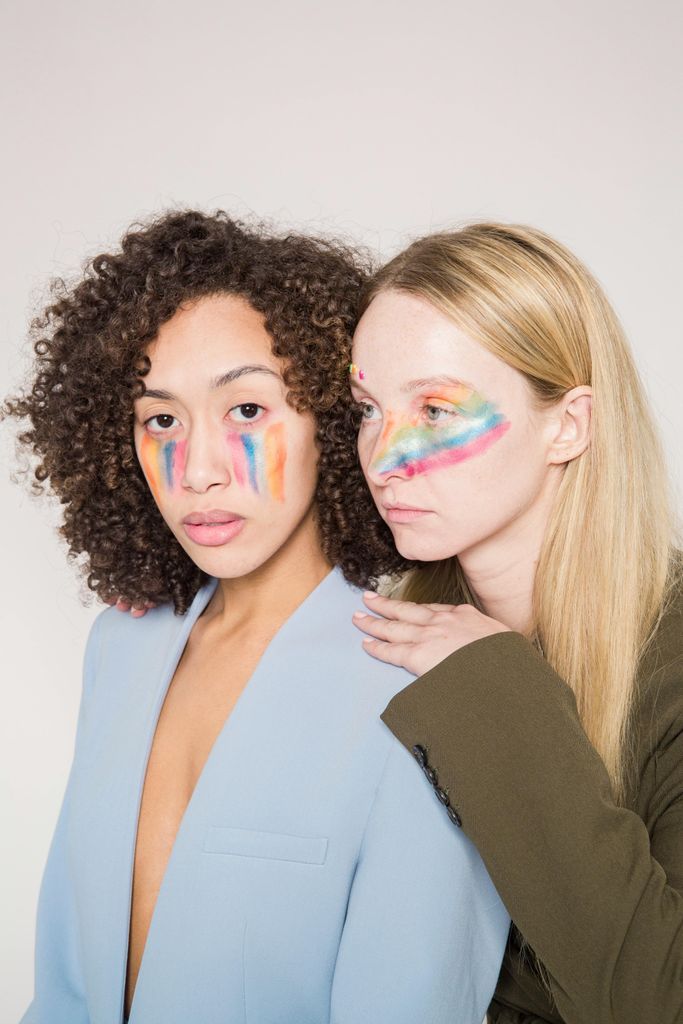 Serious multiracial women models with creative colorful makeup in trendy jackets against light background in studio