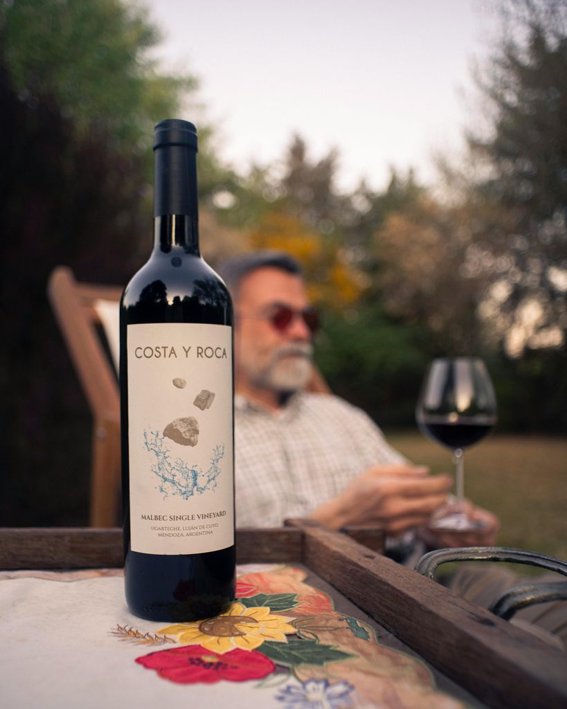 A man sitting on a wooden bench with a bottle of wine