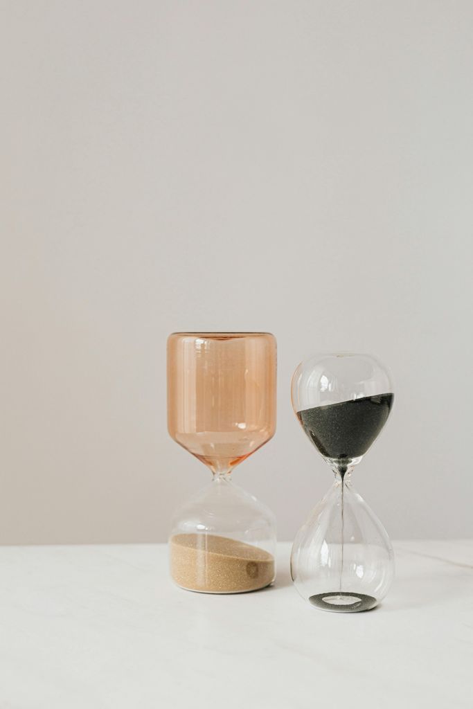 Amber and transparent hourglasses with rose and black sand placed on white table