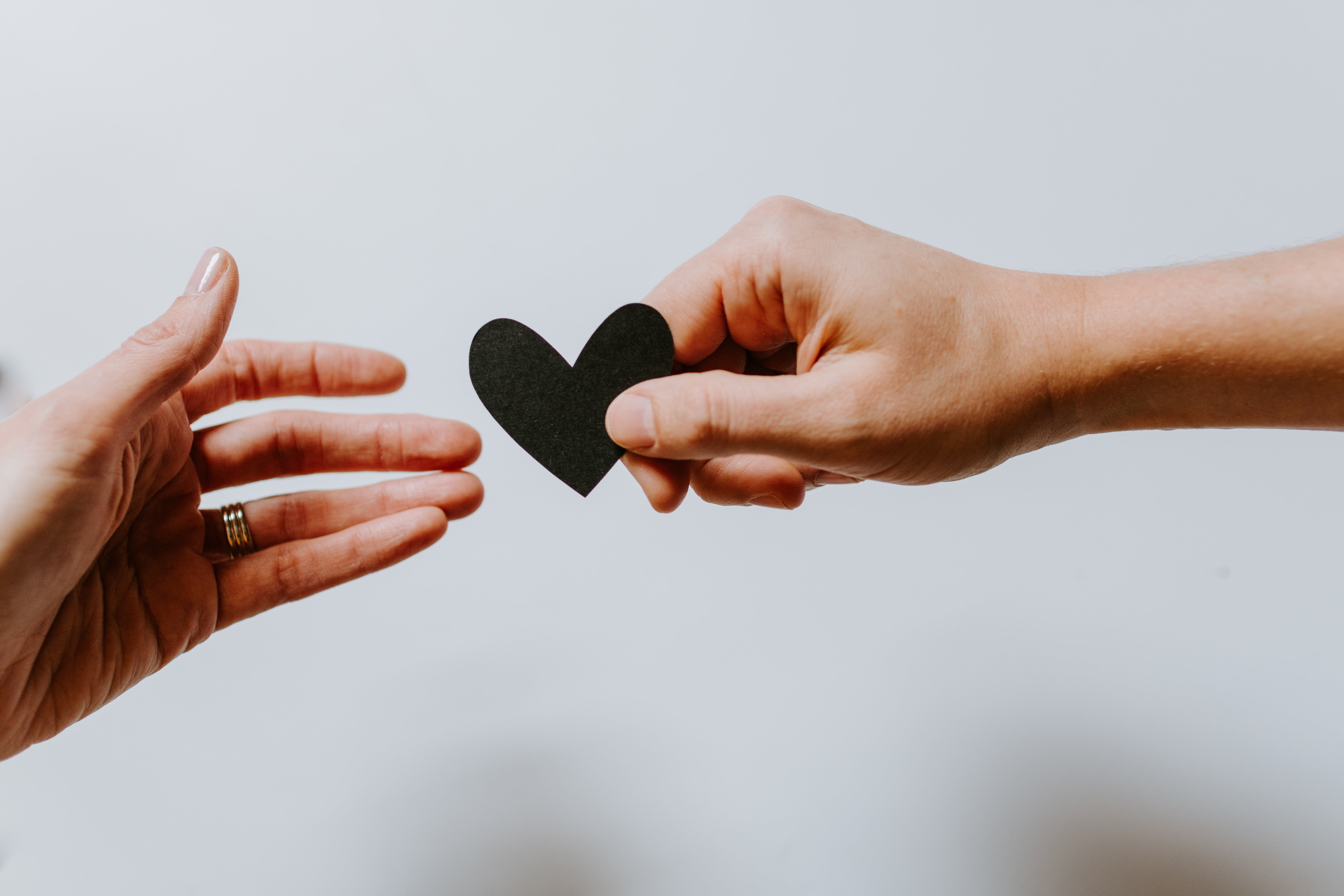 Hand passing black heart to other person's hand