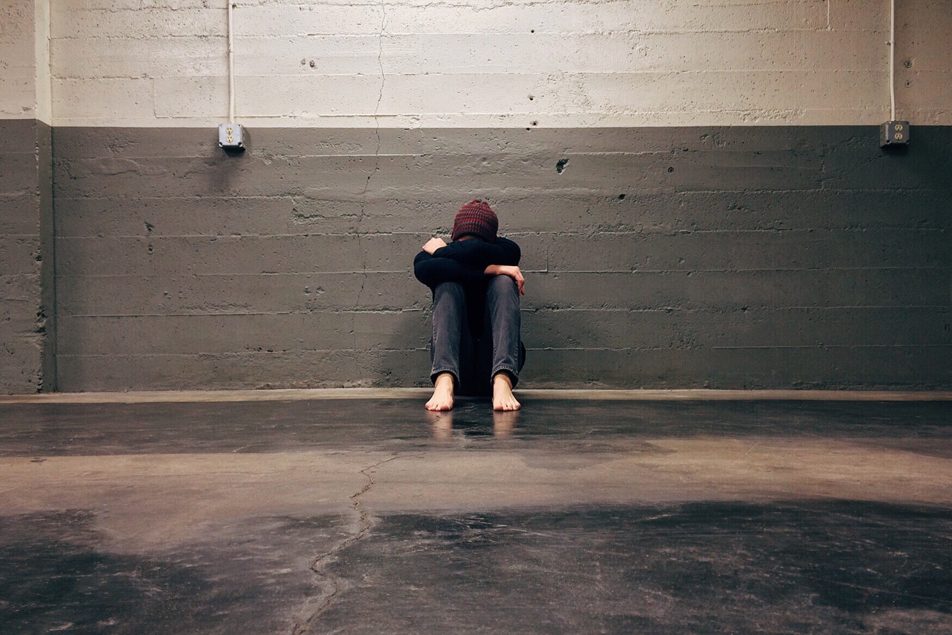 Depressed man sitting against wall alone