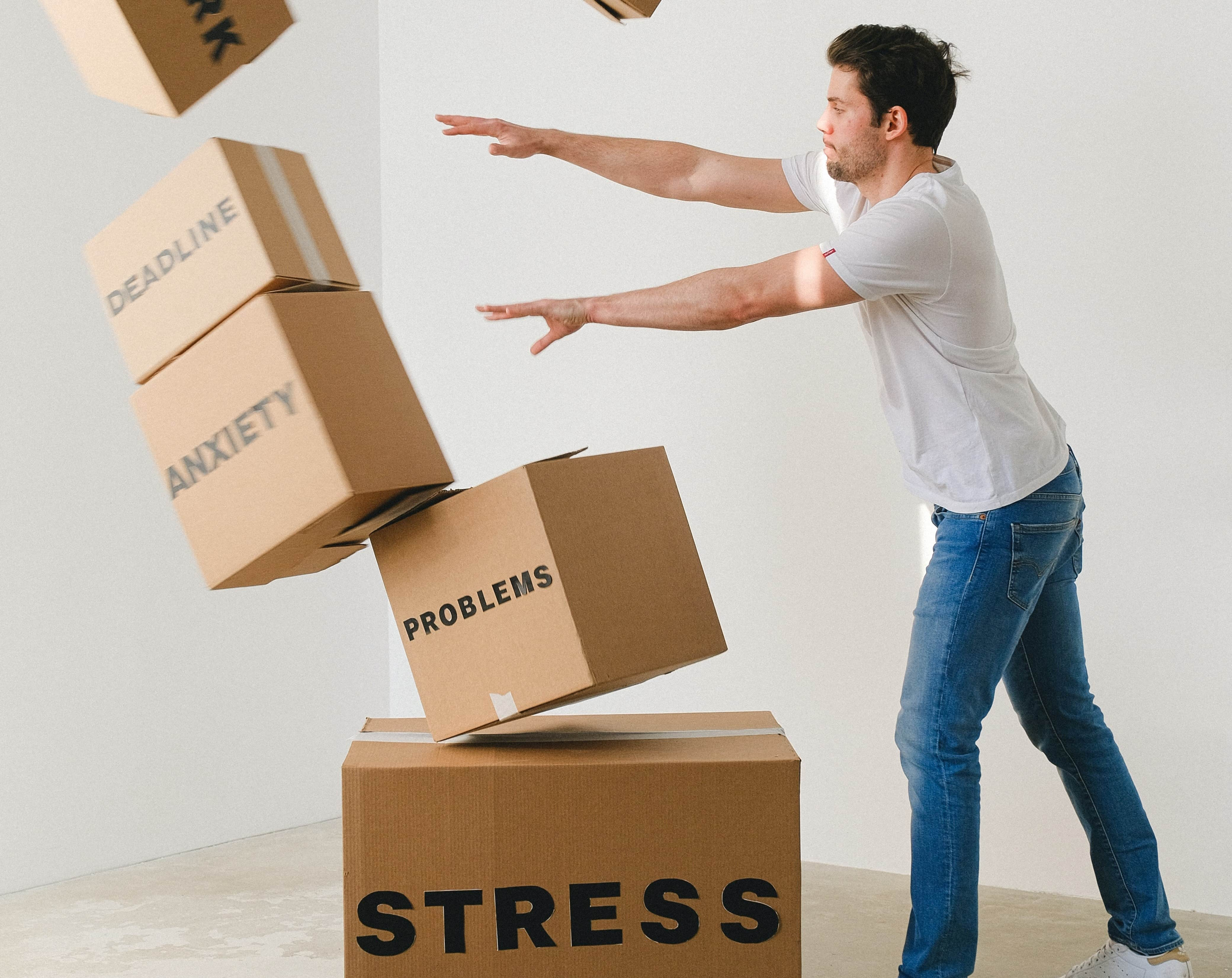 Man breaking tower of cardboard boxes with different stress-related themes written on them.